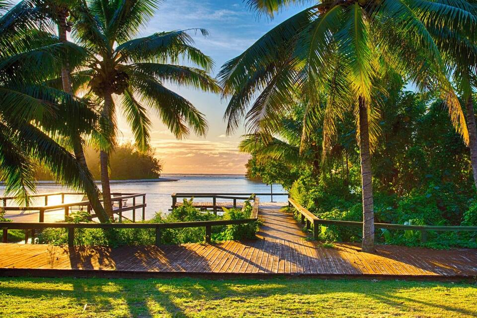 A wooden boardwalk leading to a beach with palm trees and a sunset in the background.