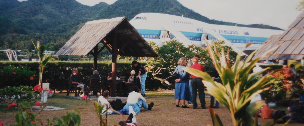 A group of people gathered around a wooden structure in a garden with a large airplane in the background.