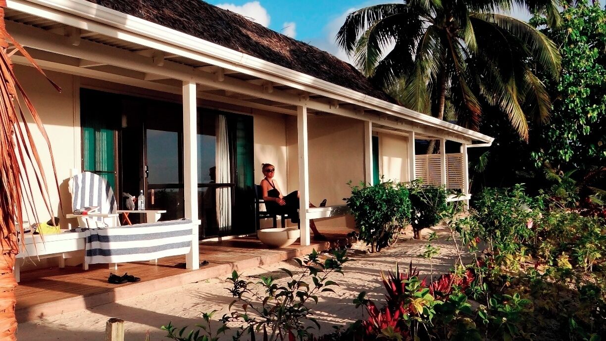 A beach house with a thatched roof, a porch, and a pool.