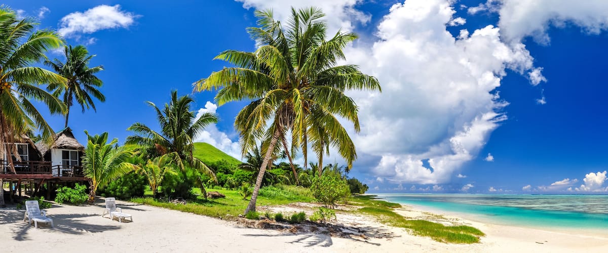 Stunning wide angle view of a beautiful beach on the remote island of Aitutaki, north of the main island Rarotonga, Cook Islands. White sand beach, shallow water, palm trees and a bungalow resort.