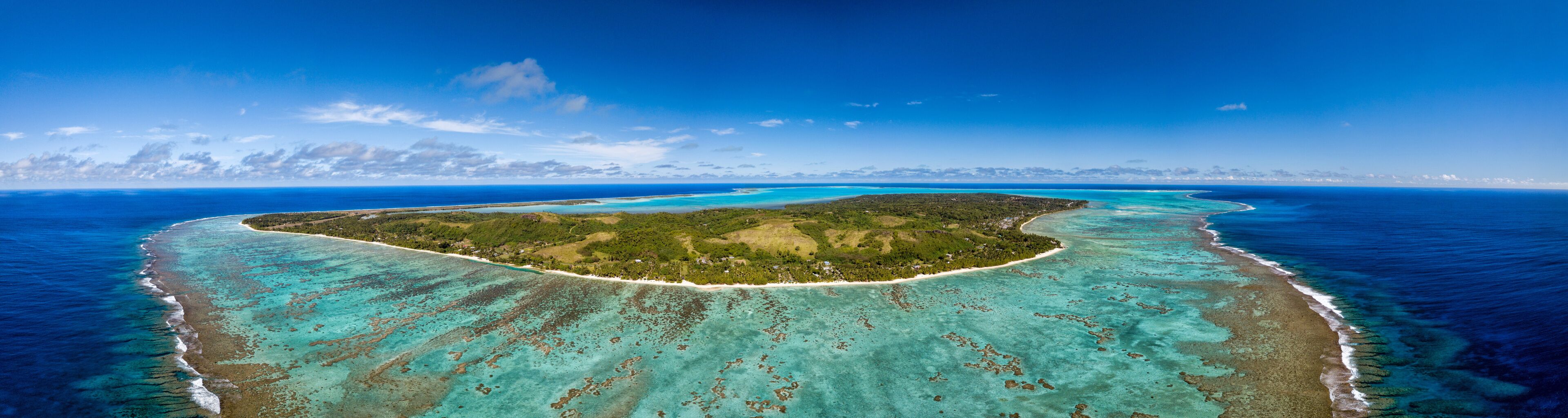 A tropical island surrounded by turquoise waters with clear skies.
