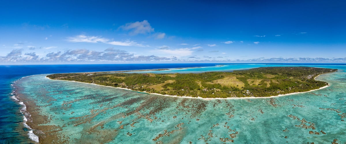 Eine tropische Insel, umgeben von türkisfarbenem Wasser und blauem Himmel.