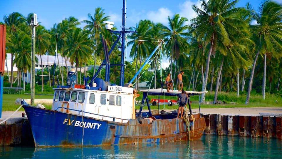 A rusted blue boat named F.V. BOUNTY docked at a pier with palm trees and a clear sky in the background.