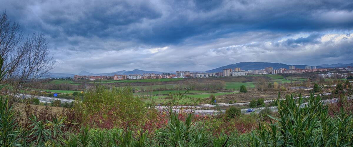 A cityscape with a highway, green fields, and mountains in the background.
