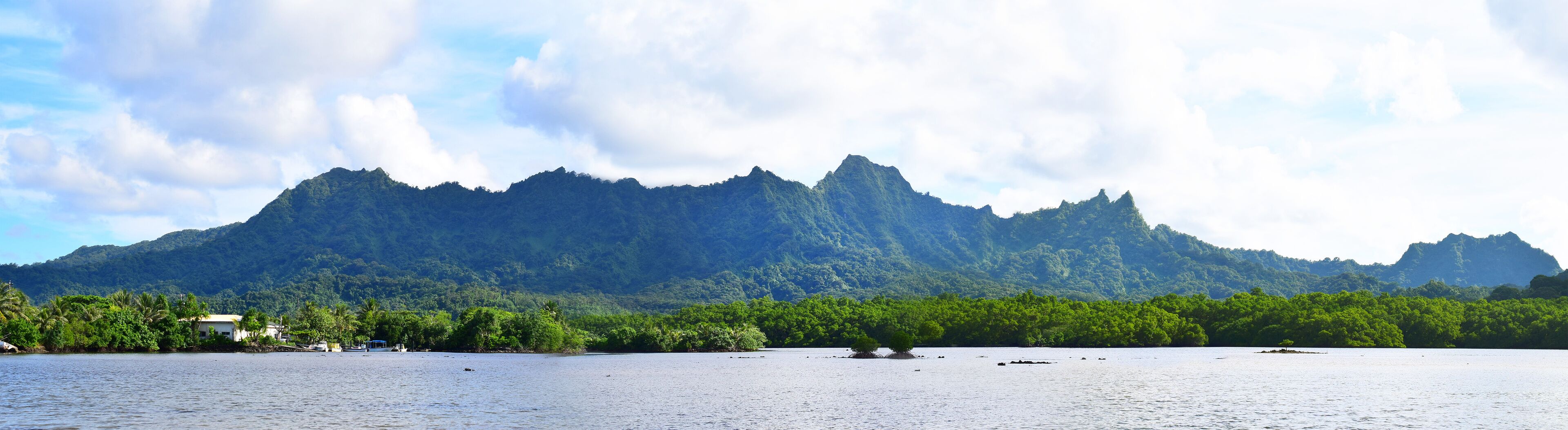 A calm lake with a mountain range in the background and a small island with vegetation in the foreground.
