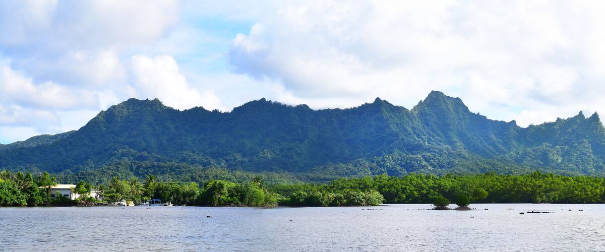 A calm lake with a mountain range in the background and a small island with vegetation in the foreground.
