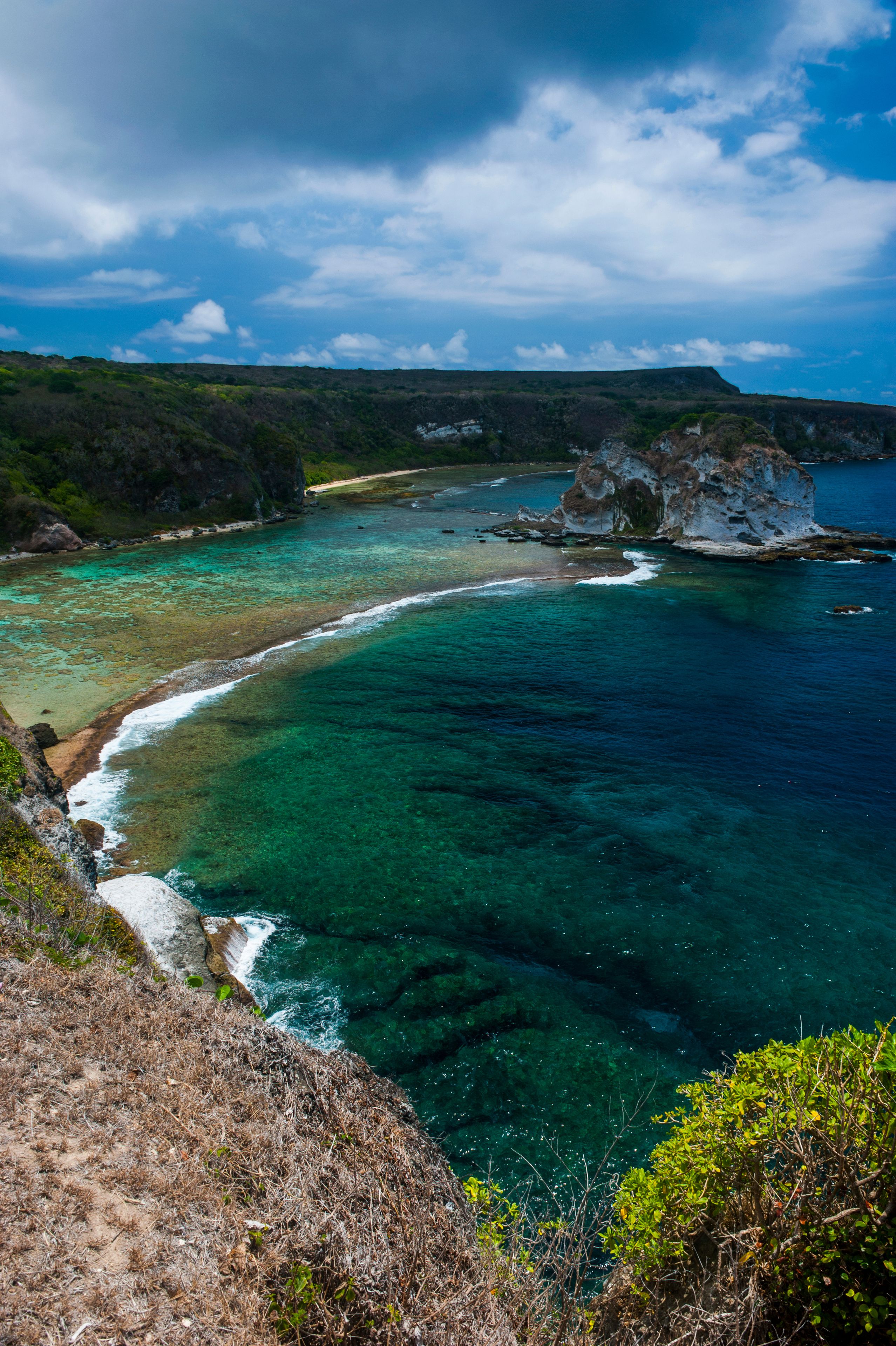 Un paysage côtier caractérisé par des eaux turquoise limpides, des falaises rocheuses et une plage de sable.