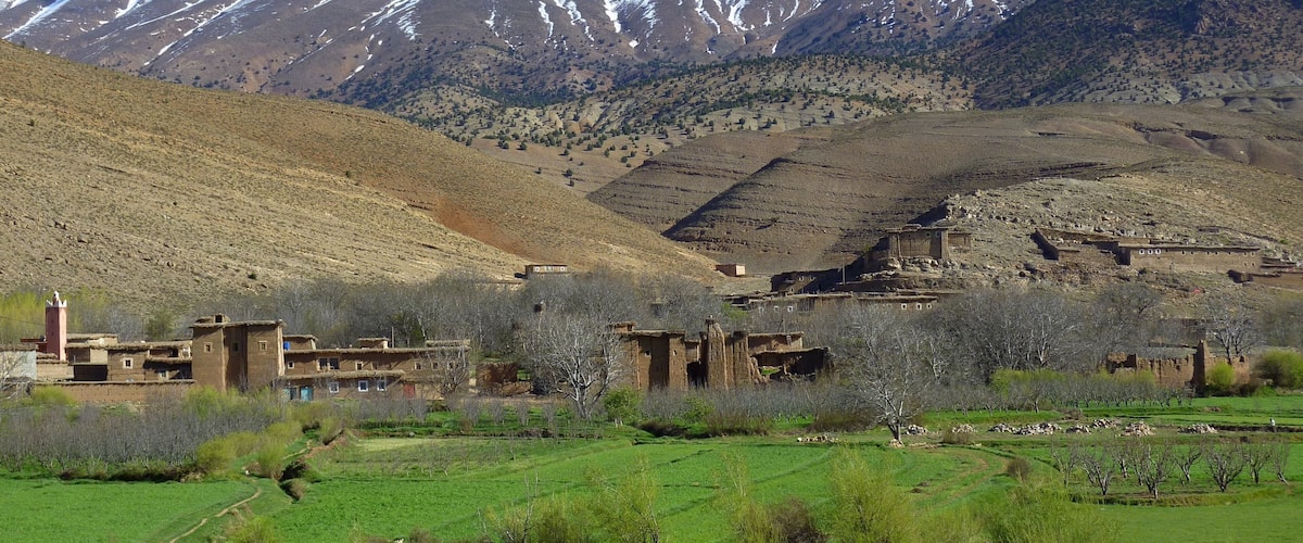 A mountainous landscape with snow-capped peaks, a valley with traditional buildings, and a green field.