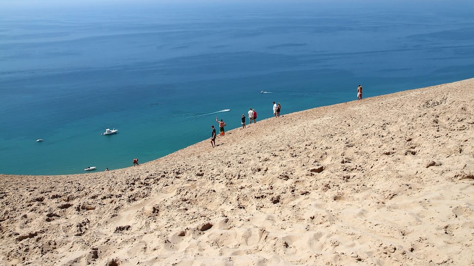 A sandy beach with people standing on the slope overlooking the sea.