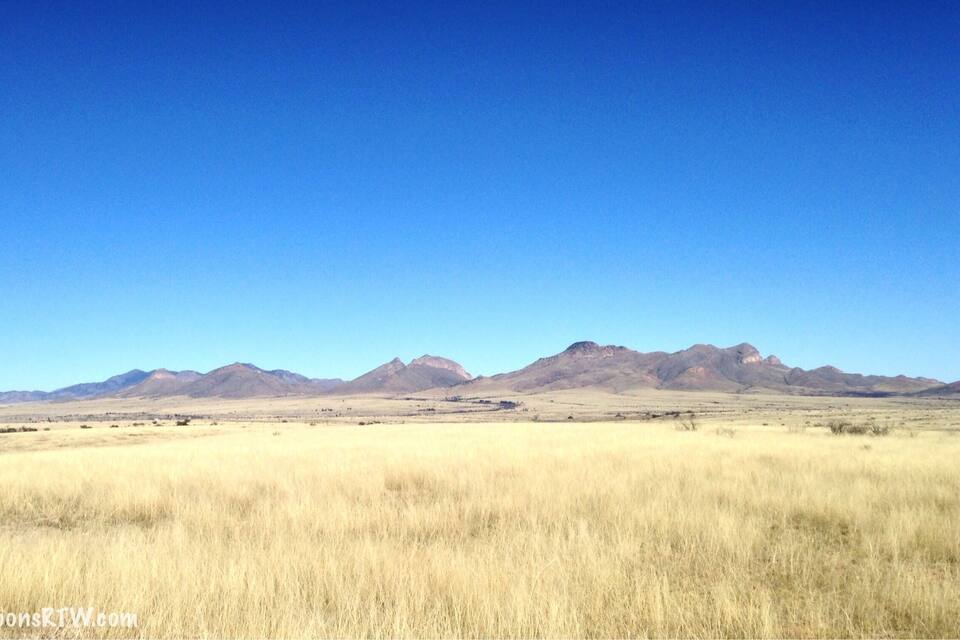 A vast, flat grassland with distant mountain ranges under a clear blue sky.