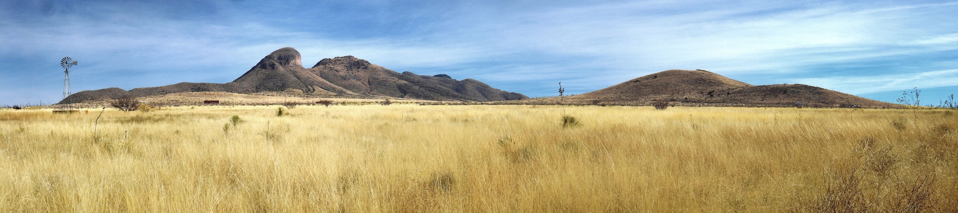 Un molino de viento, un campo cubierto de hierba y una cadena montañosa.