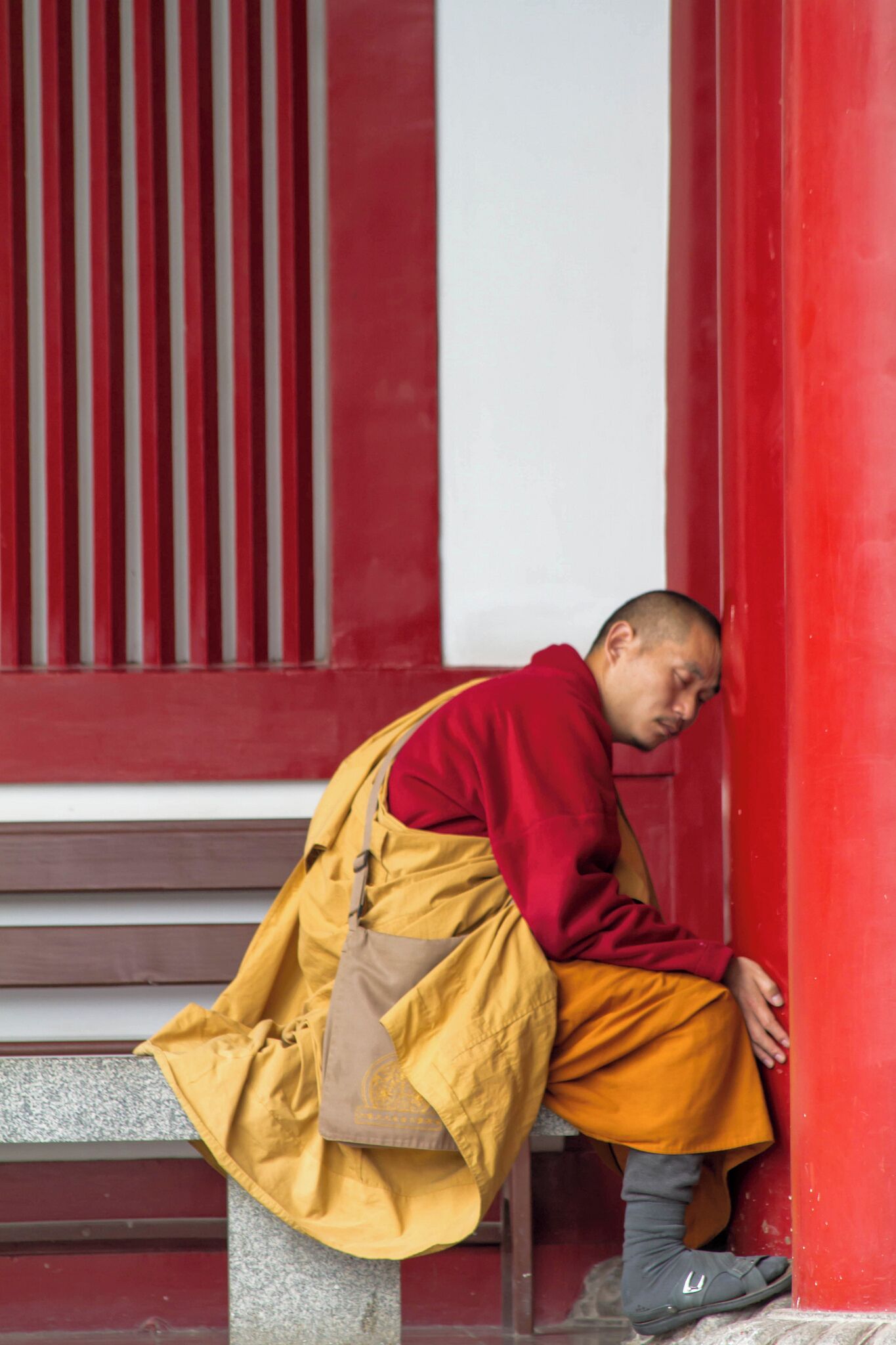 A person in traditional attire sitting on a bench against a red wall.