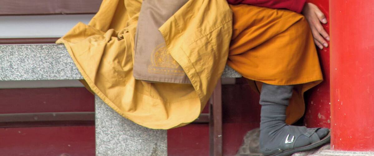 A person in traditional attire sitting on a bench against a red wall.