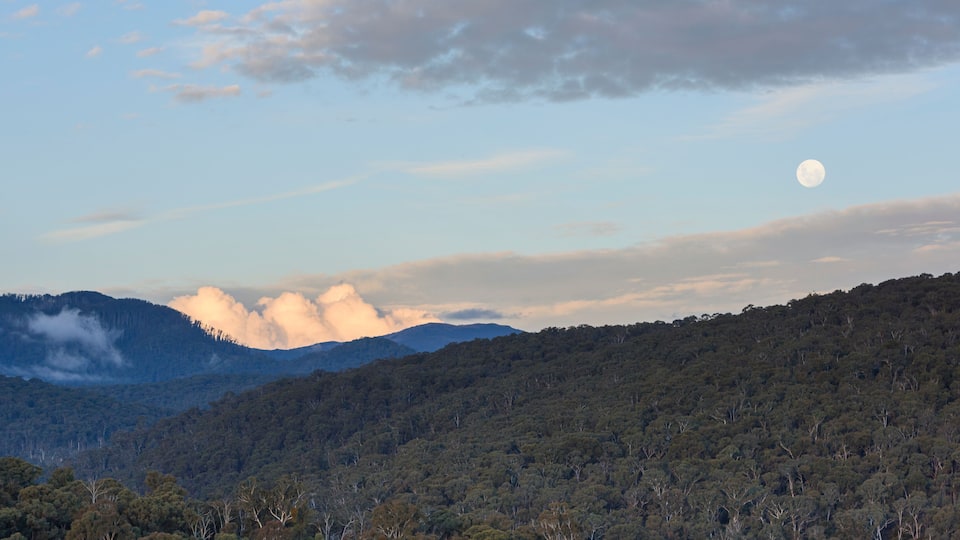 A mountain range with a full moon in the sky.