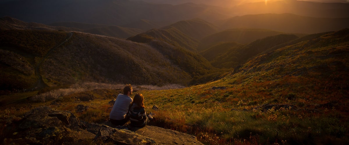 A couple sitting on a rock overlooking a valley with a sunset in the background.