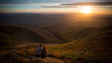 A couple sitting on a rock overlooking a valley with a sunset in the background.