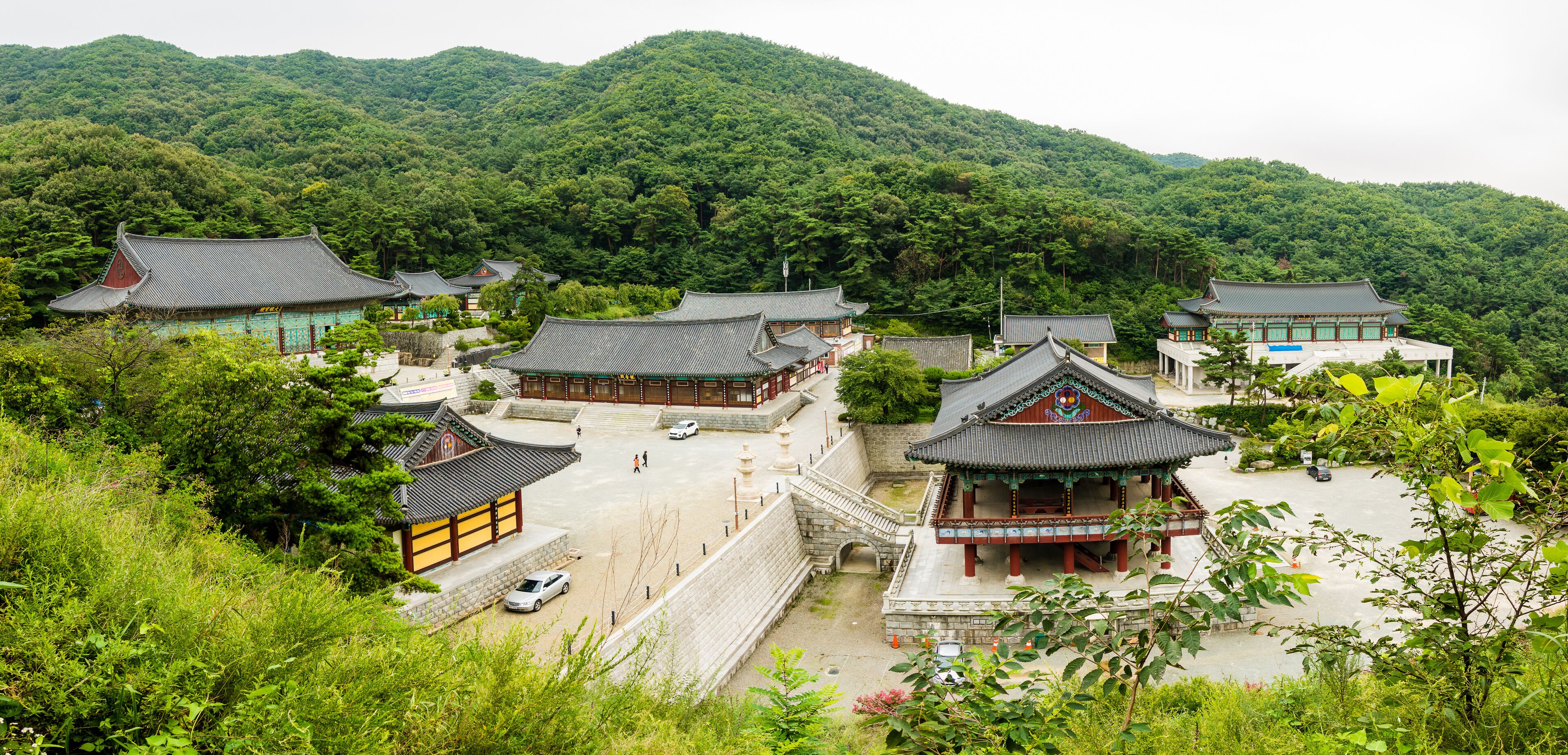 A traditional Korean temple complex with multiple buildings, surrounded by lush greenery and hills.