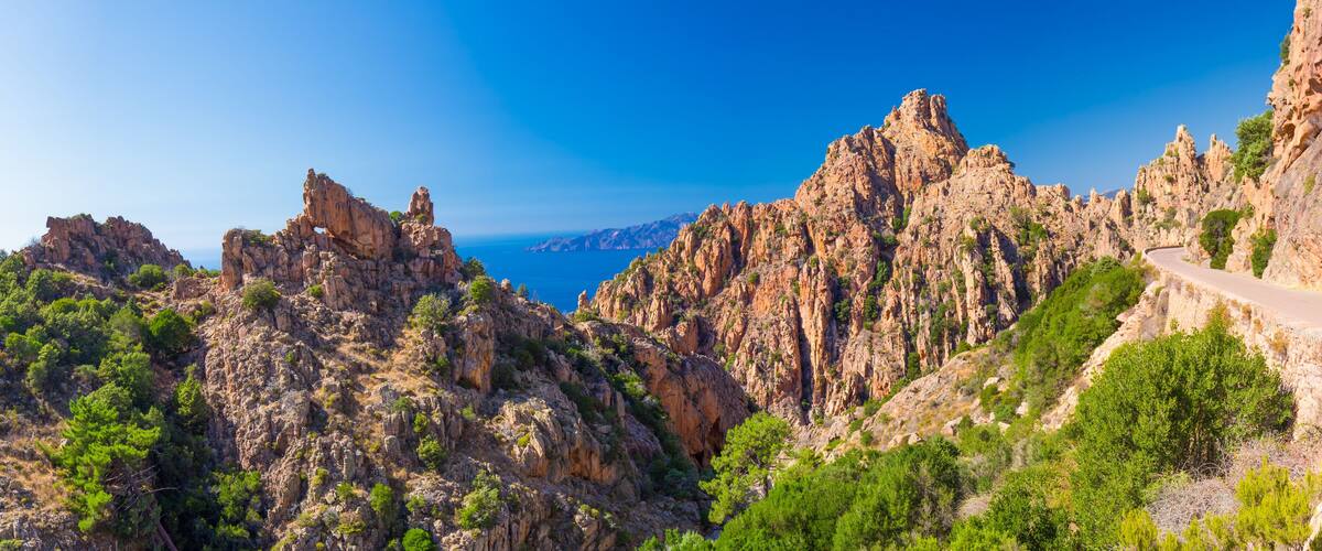 A rugged mountainous landscape with a winding road and dense greenery.