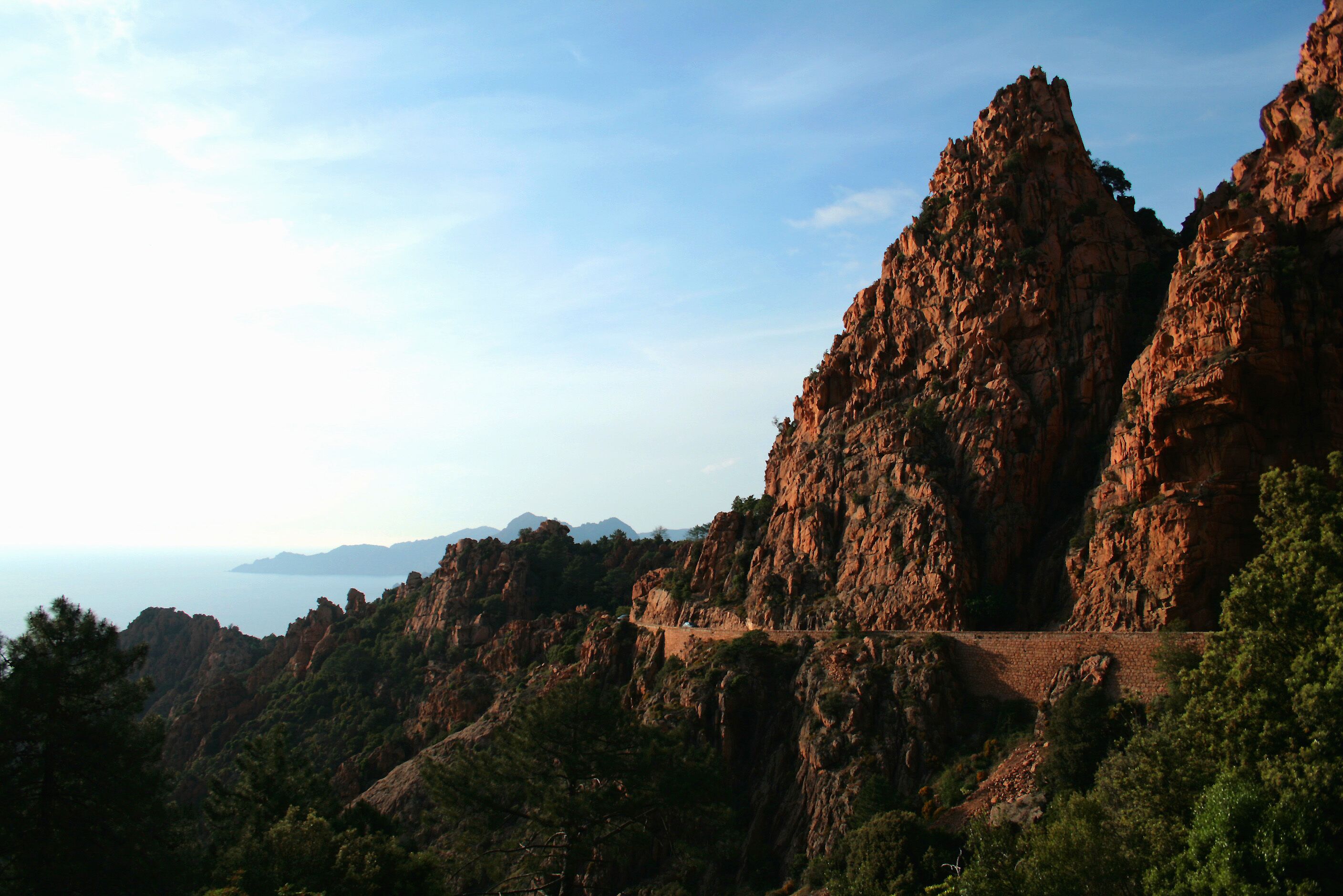 A rugged mountain landscape with a winding road and a view of the sea in the distance.