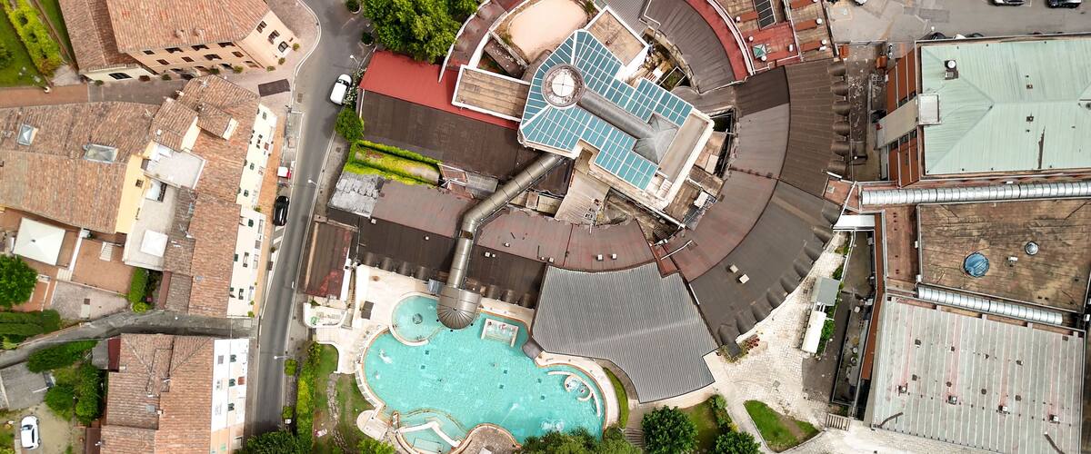 An aerial view of a residential area with a swimming pool, a large building with a red roof, and surrounding greenery.