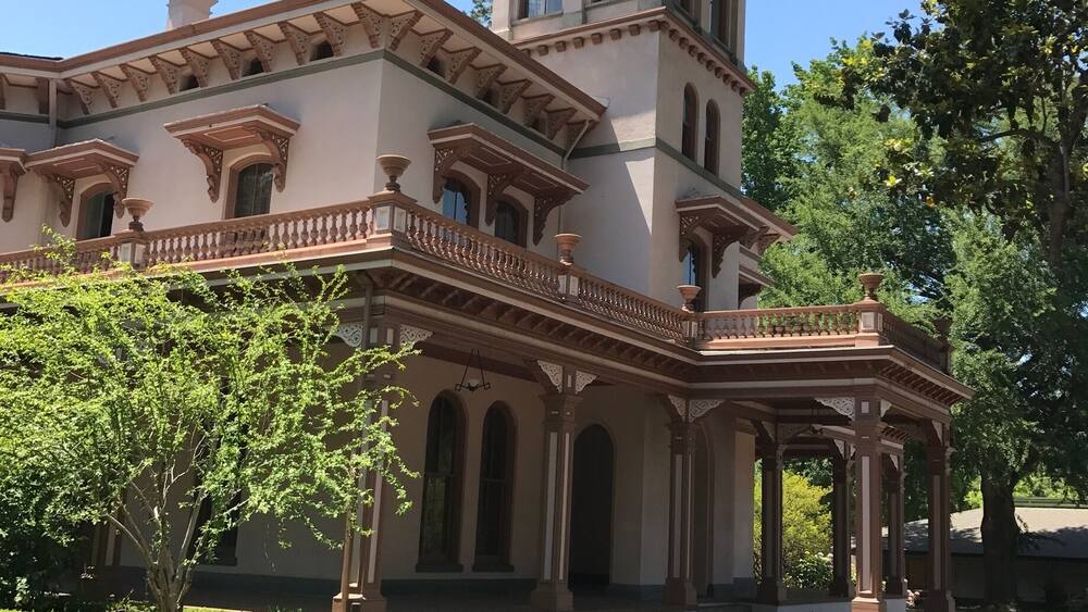 Ein großes, historisches Gebäude mit einem Turm, Rundbogenfenstern und einer Veranda.