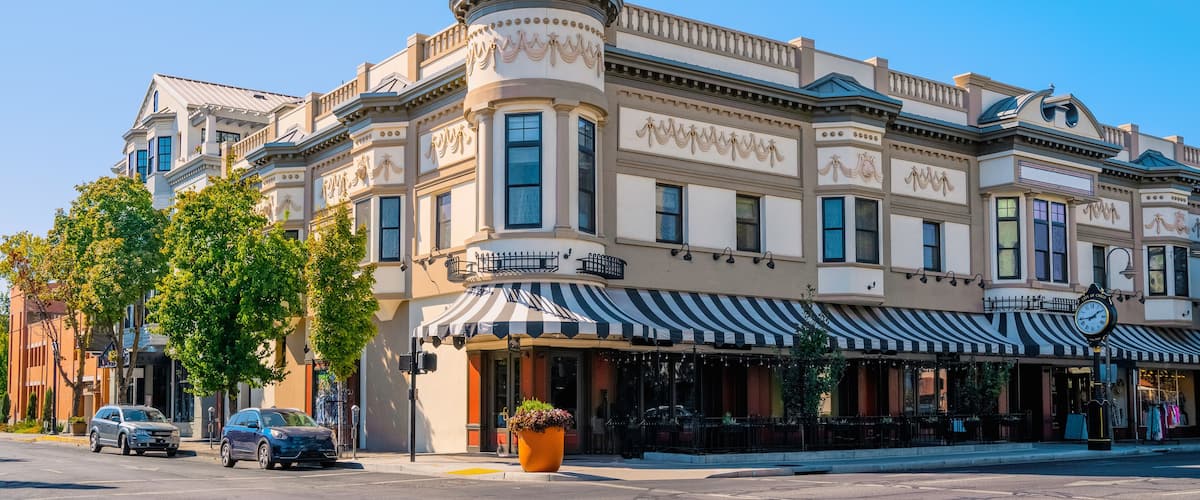 A historic building with a tower, striped awning, and parked cars.
