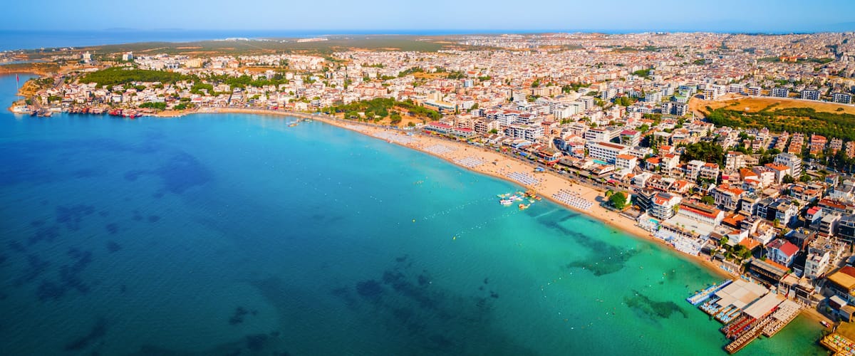 An aerial view of a coastal city with a beach, dense urban area, and clear blue waters.