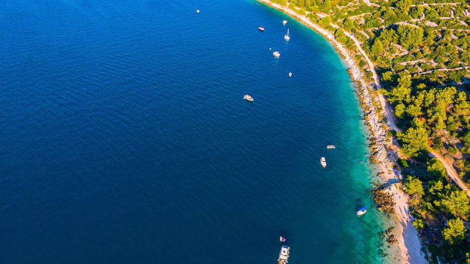 A coastal area with clear blue waters, boats, and a densely wooded shoreline.