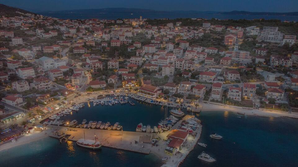 A coastal town at dusk with a marina, buildings, and a moon in the sky.