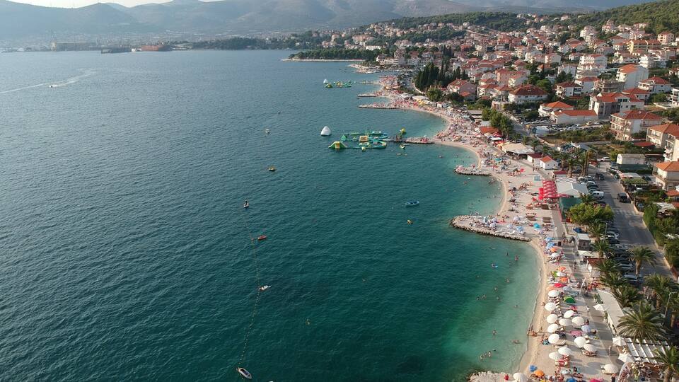 A coastal town with a beach, boats, and a mountainous backdrop.