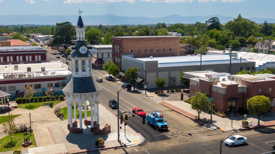 A town square with a clock tower, a fire truck, and a street with cars.