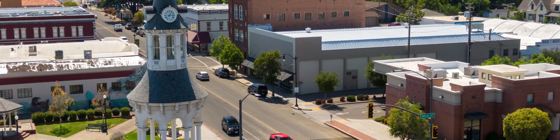 Aerial view of Red Bluff town square, showing a clock tower, businesses, and traffic. Cars and a utility truck are visible on the street. The Cone & Kimball Tower, Red Bluff, California, USA
