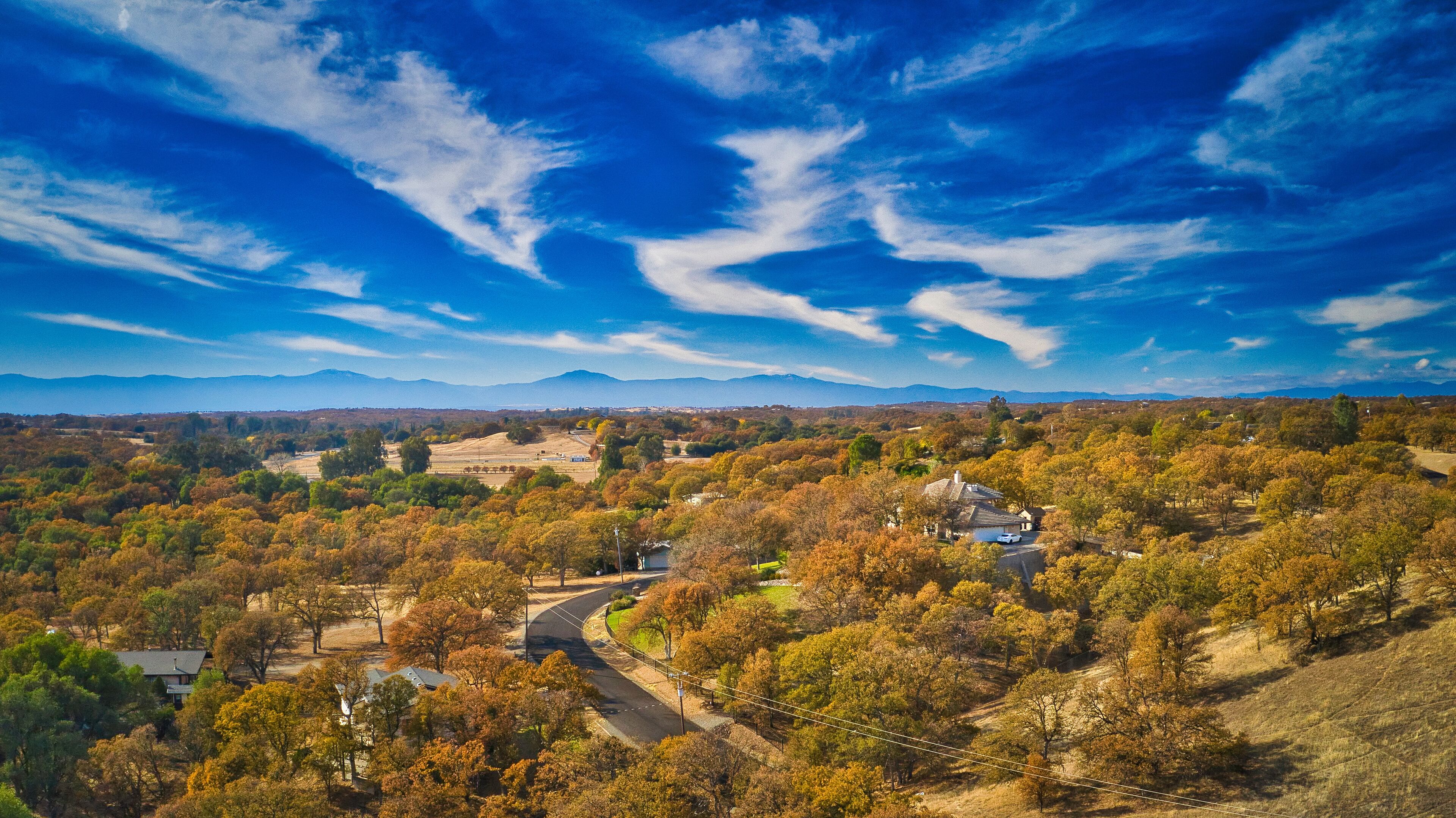 A valley with autumn foliage, a winding road, and distant mountains under a blue sky.