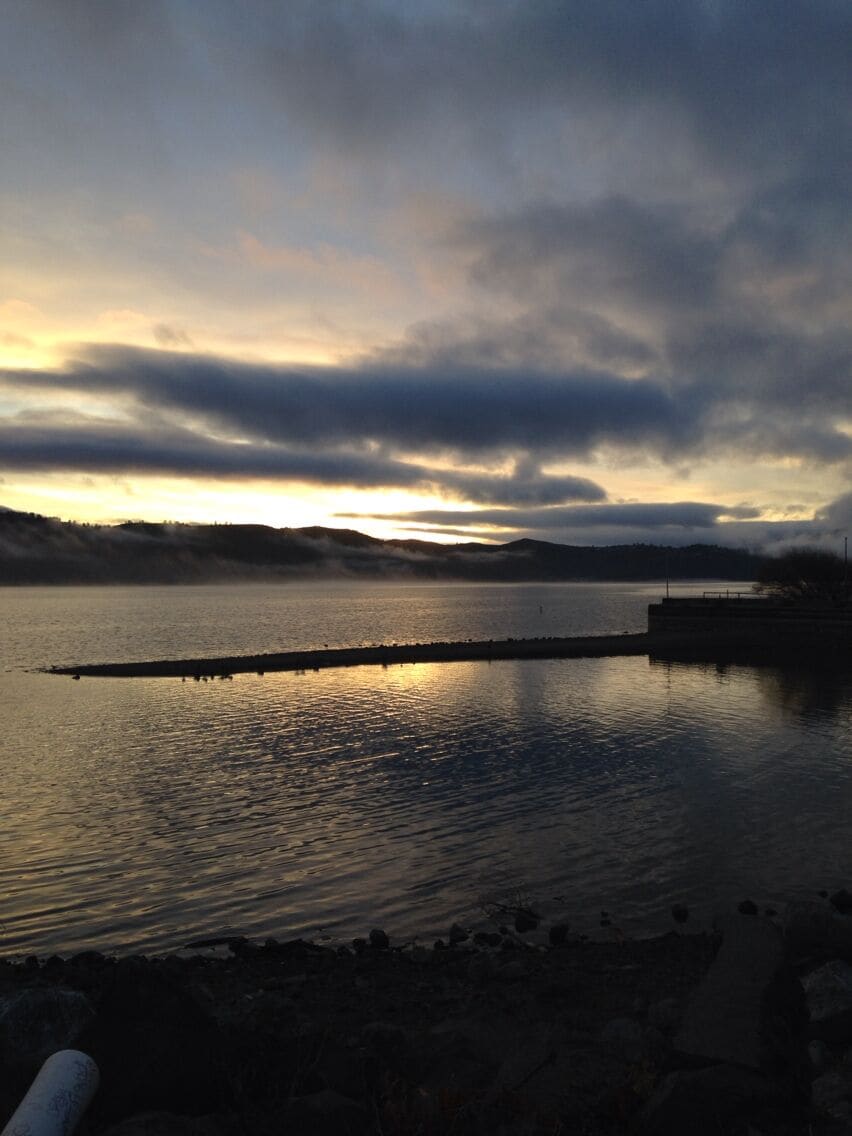 A calm lake at sunset with a dock extending into the water.