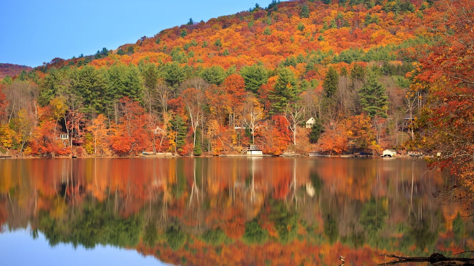 A lake reflecting autumn foliage, with a hill in the background and a small house near the water's edge.