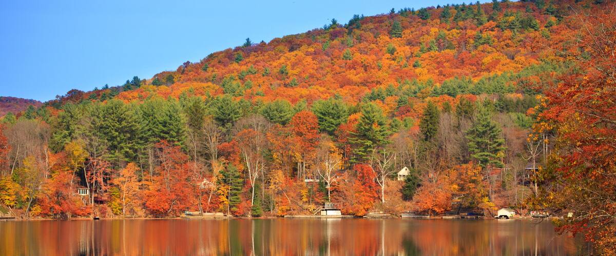 A lake reflecting autumn foliage, with a hill in the background and a small house near the water's edge.