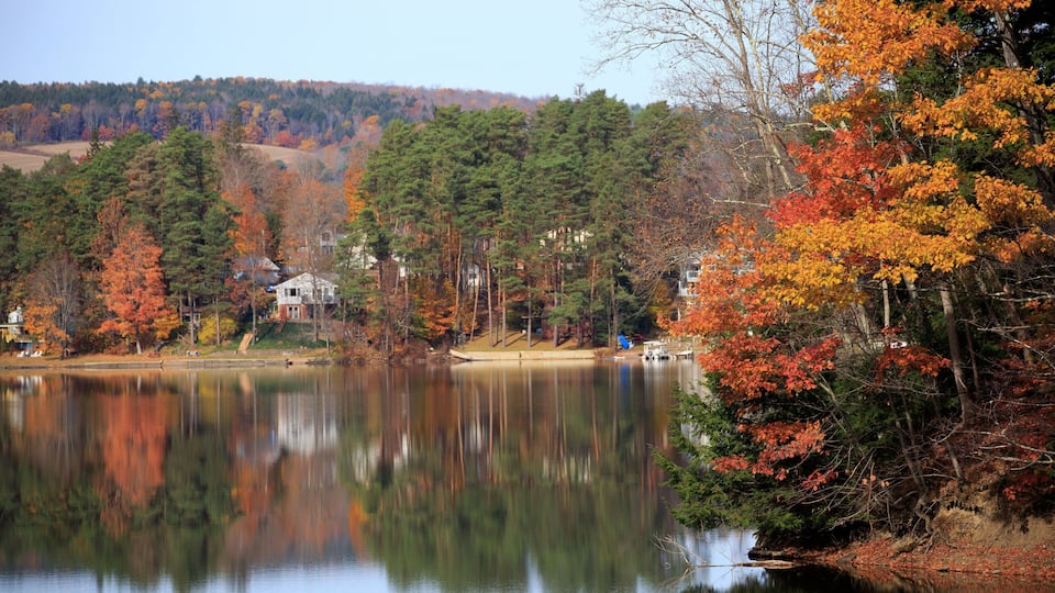 A calm lake surrounded by autumn-colored trees and a distant house.