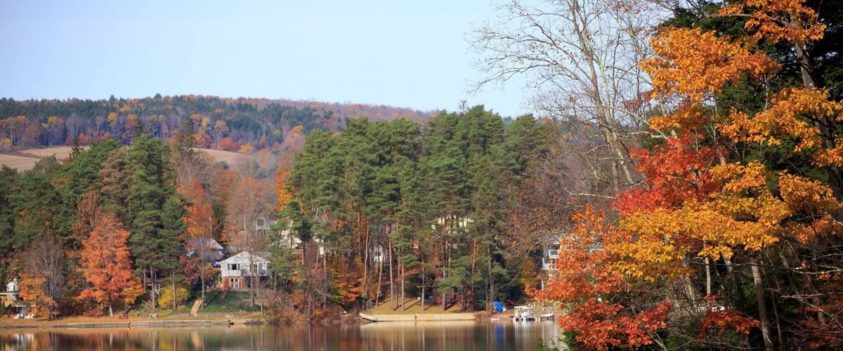 A calm lake surrounded by autumn-colored trees and a distant house.