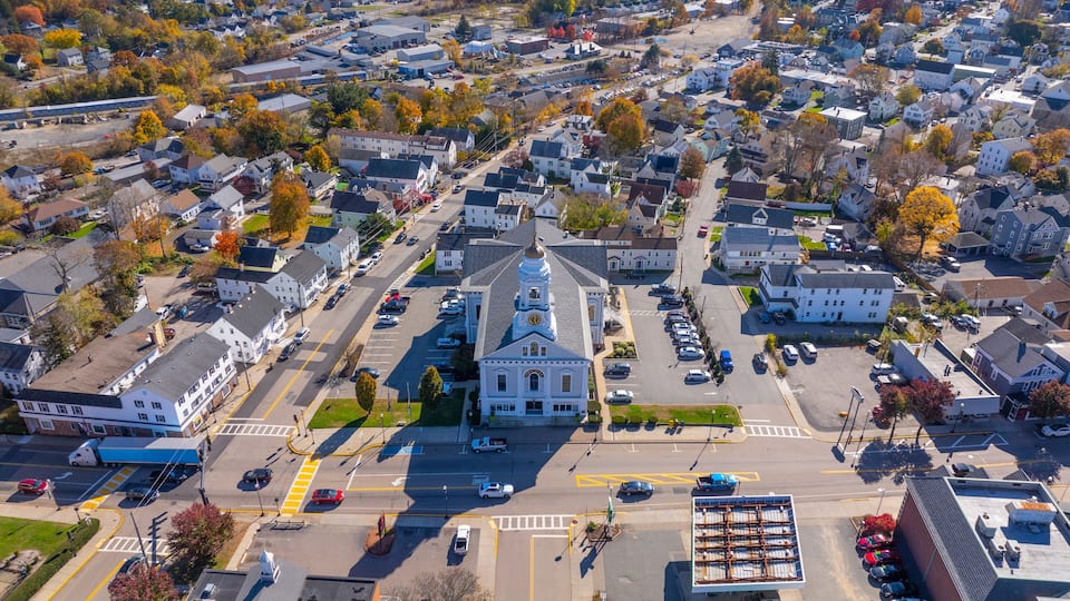 An aerial view of a town with a prominent church, residential houses, and a parking lot.