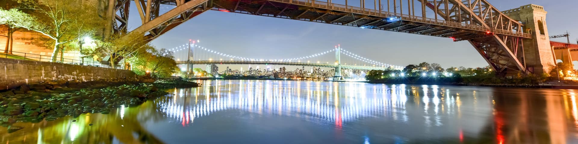 A steel bridge arching over a river with city lights reflecting on the water.