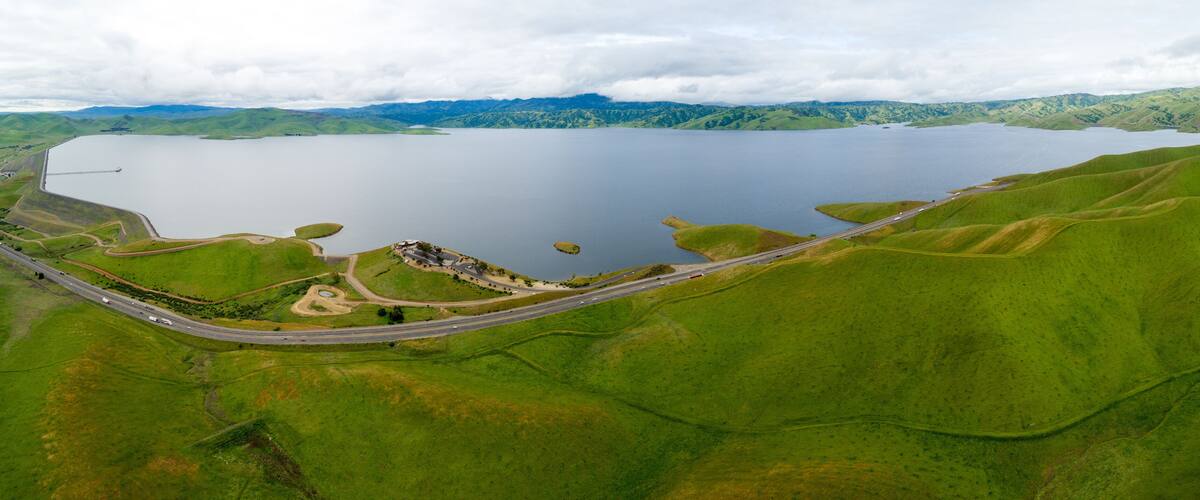 A large lake surrounded by green hills, a winding road, and a small settlement.