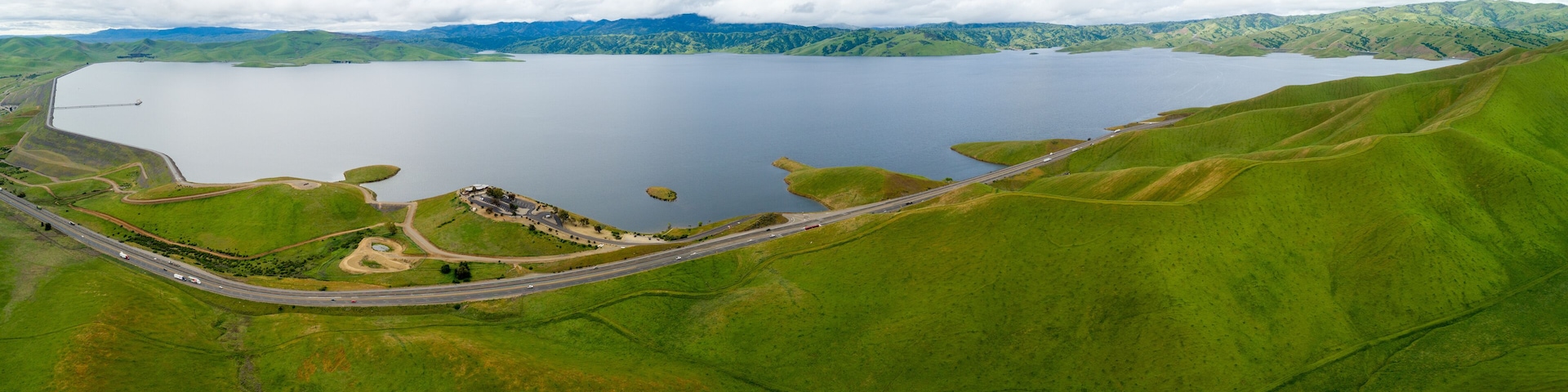 A large lake surrounded by green hills, a winding road, and a small settlement.