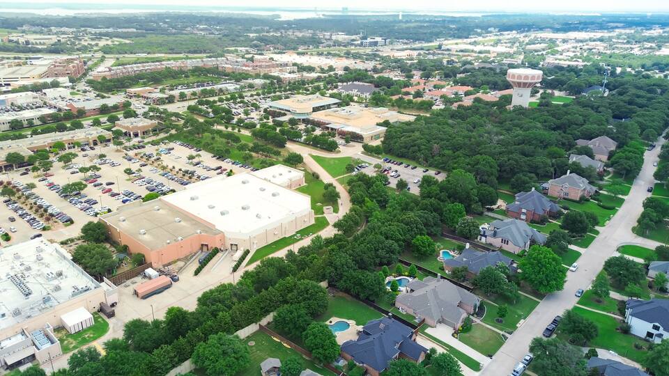 An aerial view of a suburban area with a large parking lot, residential houses, and a prominent water tower.