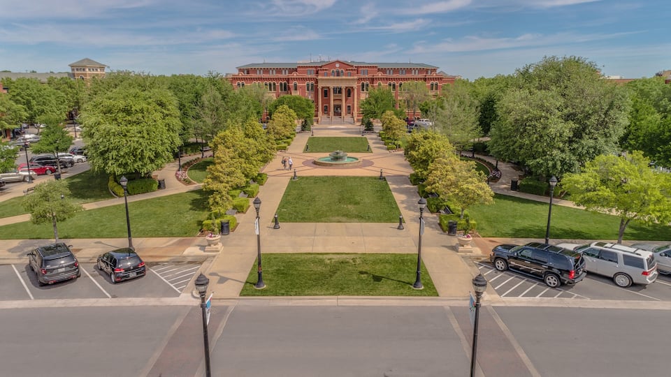 A large red brick building with a central courtyard, surrounded by trees and a parking lot.