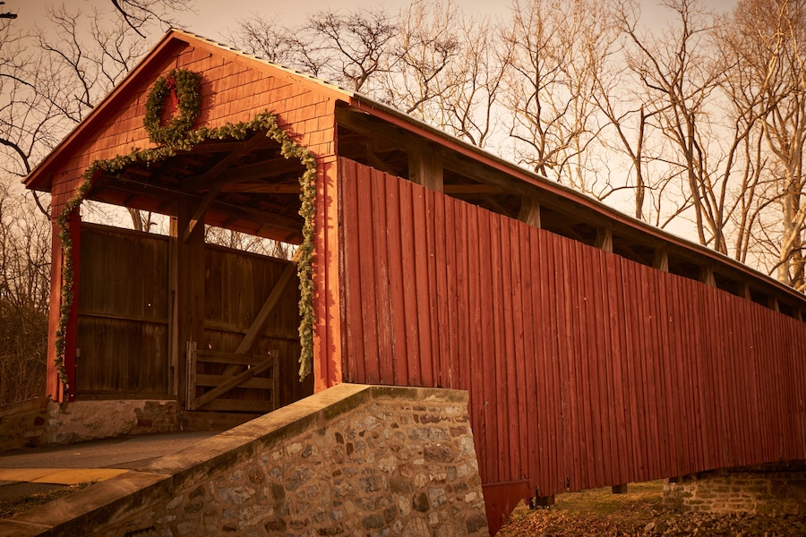 A red covered bridge with a stone foundation, a wooden door, and a wreath on the roof.
