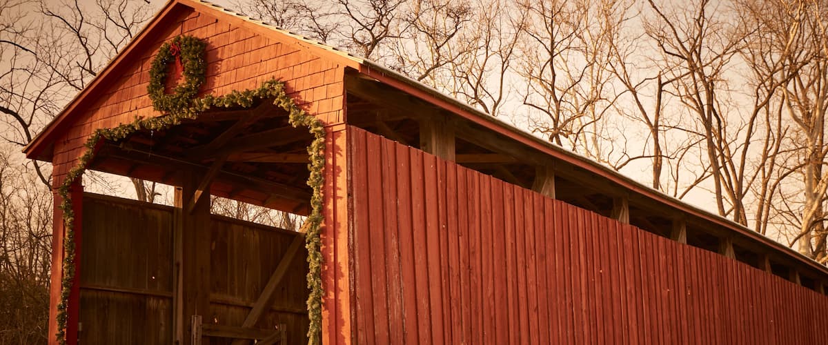 A red covered bridge with a stone foundation, a wooden door, and a wreath on the roof.