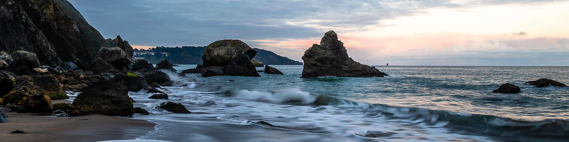 A rocky coastline with waves crashing against the shore and large boulders in the water.