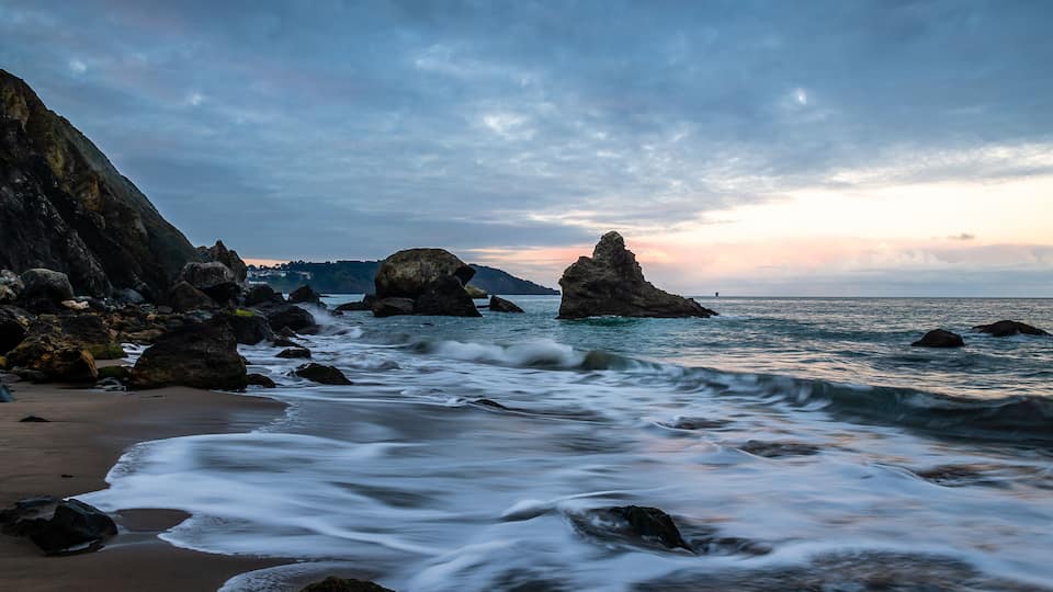 A rocky coastline with waves crashing against the shore and large boulders in the water.