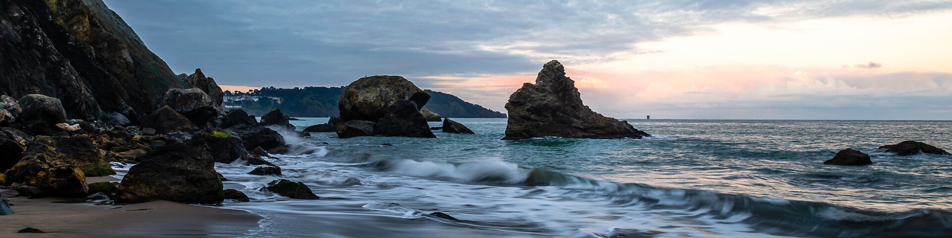 Una costa rocosa con olas rompiendo contra la orilla y grandes rocas en el agua.