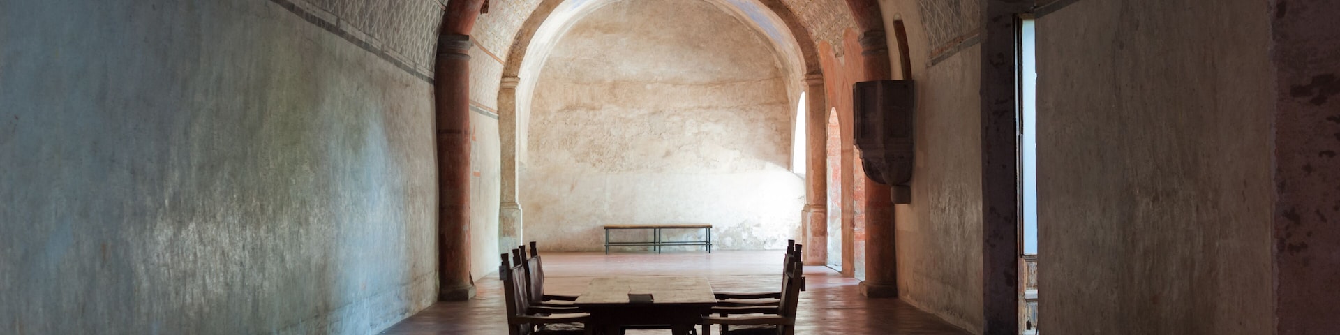 Un pasillo con una mesa y sillas de madera, techo abovedado y paredes con diseño.